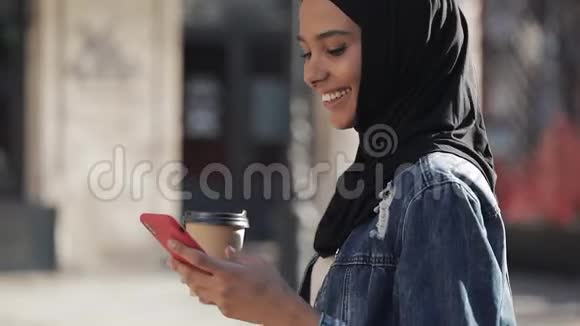 微笑穆斯林妇女戴头巾在市中心散步使用智能手机和喝咖啡视频的预览图