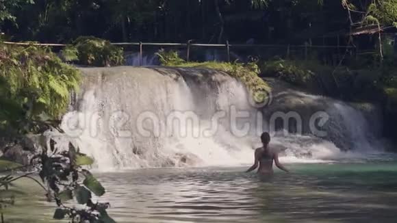 年轻女子在热带森林的瀑布里洗澡溪水溅在背景上流动水浇注量视频的预览图