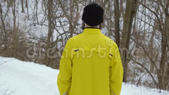 穿黄色运动外套的人站在冬季森林的山上的后景视频的预览图