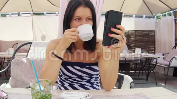 美女在咖啡馆喝茶看电话视频的预览图