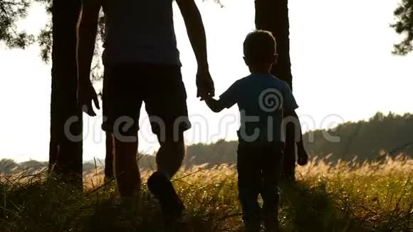 一对年轻的父子在日落时分穿过树林的剪影两个旅行者特写概念视频的预览图