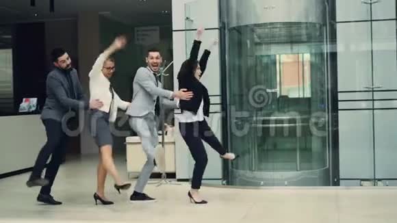 爆笑的男女商人们在办公室聚会上玩得很开心在大厅里跳舞一起享受音乐和视频的预览图