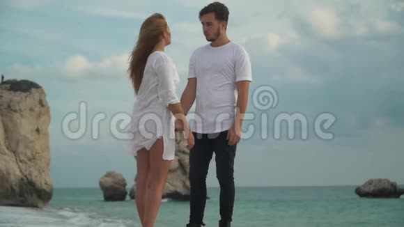 一对年轻夫妇站在岩石海岸边慢镜头交谈男人和女人握着对方的手闲暇视频的预览图