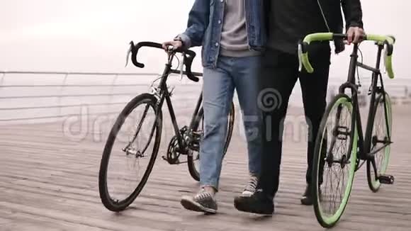 在秋日现代年轻的时髦夫妇和他们的自行车一起在海边散步拥抱走在木头上视频的预览图