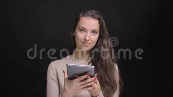 年轻的黑发白种人长头发的白种人女孩高兴地将绿色的平板电脑屏幕显示在黑色相机上的肖像视频的预览图