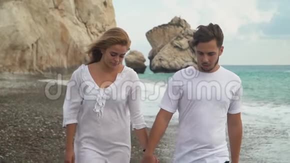 一对穿着白色衣服的年轻夫妇在海边或海边的岩石海岸散步彼此拥抱着交流视频的预览图