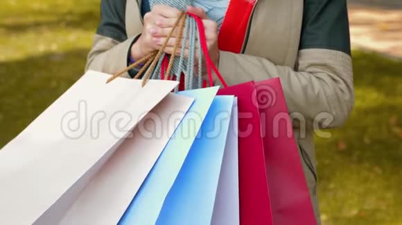 一个女孩站在公园里用多种颜色的纸袋购物视频的预览图