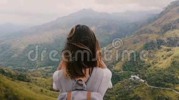 后景兴奋的旅游女子背着背包头发随风飘动沉思看着史诗般的山景视频的预览图