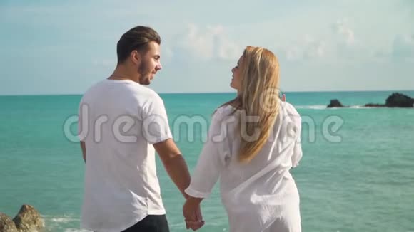 年轻夫妇站在海边欣赏美丽的海景男人和女人互相牵手互相看着视频的预览图