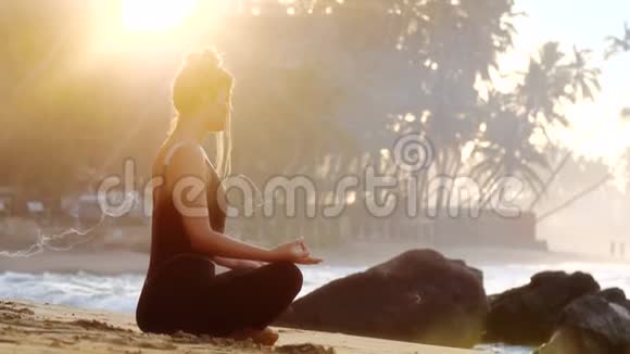 穿黑色运动服的年轻女子在沙滩上做瑜伽视频的预览图