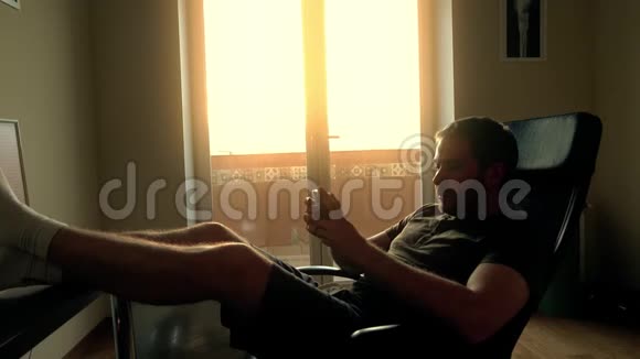 英俊的长胡子男人在家里放松在智能手机上打字视频的预览图