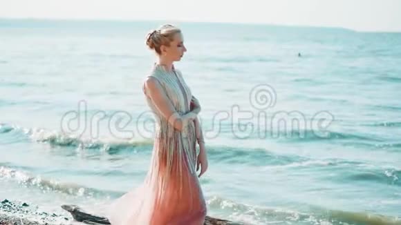 孤独的旅人穿着一件粉红色的长裙子站在蔚蓝的大海的岸边想着拥抱着自己视频的预览图