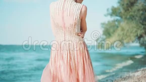 苗条的女孩站在镜头前穿着浅粉色的豪华昂贵闪亮的裙子在阳光下薄纱列车金发视频的预览图