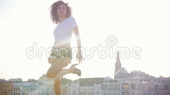 迷人的莫拉托年轻女子卷发在现代建筑的背景下跳舞明亮的阳光视频的预览图