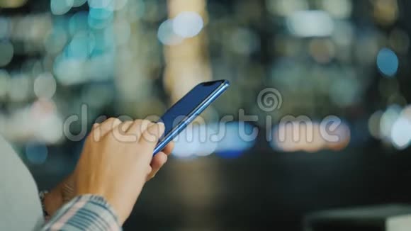 一位年轻女性的双手拿着智能手机在城市的背景分裂的灯光下视频的预览图