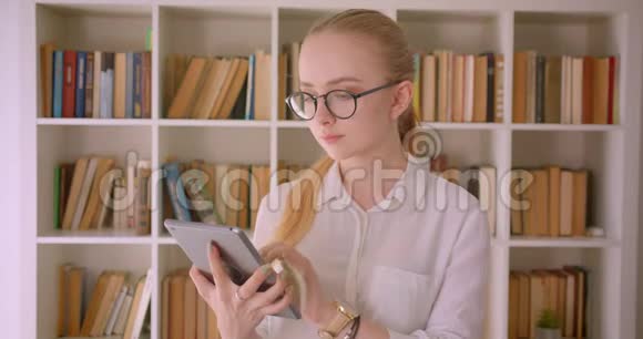 年轻漂亮的白种人金发女学生的特写肖像戴着眼镜用平板电脑显示绿色屏幕视频的预览图