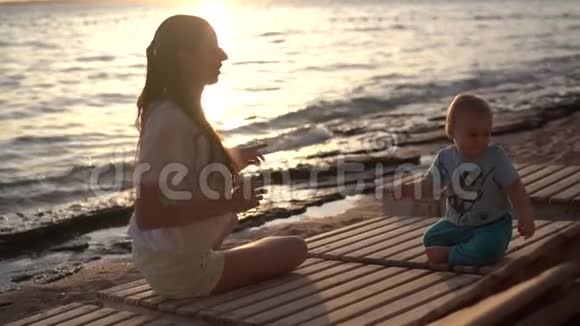 日落时女孩和小男孩坐在一个木休息室里跳舞视频的预览图