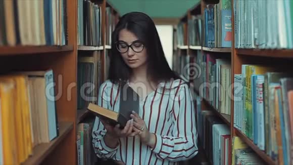 图书馆里戴着眼镜的年轻漂亮女人手里拿着一本书翻阅着书页视频的预览图