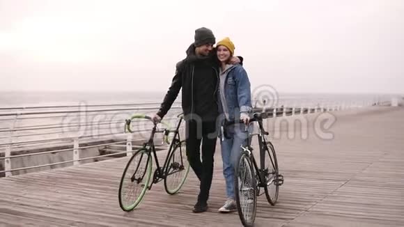 秋天一对年轻的嬉皮士们和他们的自行车一起在海边散步走在木头上视频的预览图
