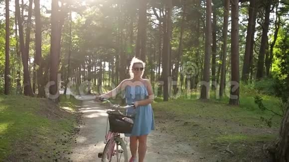 夕阳西下美丽的欧洲女人在森林里散步骑自行车在新鲜空气中散步骑自行车进来视频的预览图