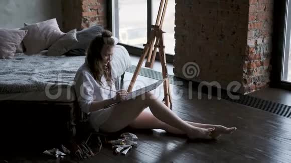 画家画了一幅坐在家里工作室地板上的画穿着男人衬衫女孩视频的预览图