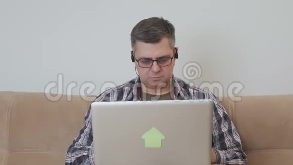 一个中年男人坐在沙发上耳朵里戴着耳机他喜欢笔记本电脑吃香蕉视频的预览图