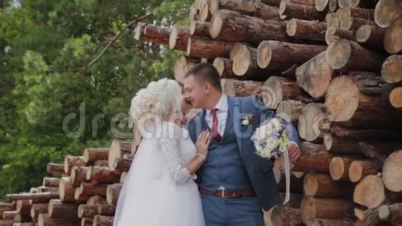 美丽的新郎和金发新娘在森林里的原木旁边拥抱和亲吻视频的预览图
