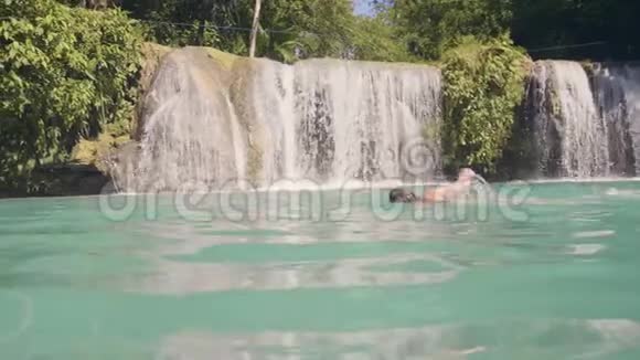 微笑的女人在热带雨林的瀑布湖里游泳快乐的女人在清澈的海水中游泳视频的预览图