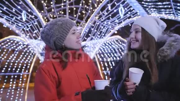 两个女孩在一个冬天的晚上漫步在市中心为圣诞节装饰了明亮的灯光和花环女孩视频的预览图