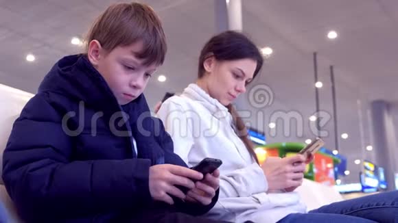 女人和她的儿子在机场大厅玩手机等待航班视频的预览图