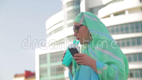 一位年轻的穆斯林妇女戴着浅色围巾和太阳镜戴着现代建筑的背景视频的预览图