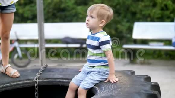 小托德勒男孩坐在公园儿童操场上的大蒂里视频的预览图