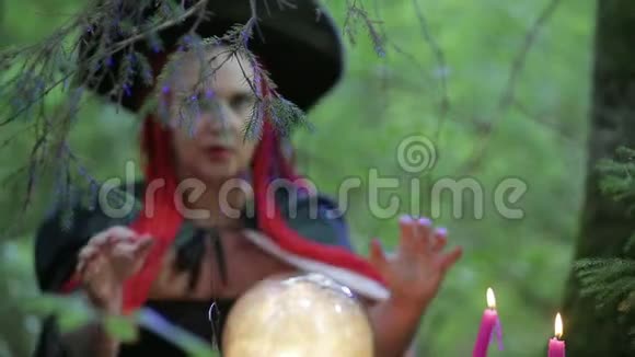一位在森林里长着红色头发的女巫用发光的球和燃烧的蜡烛做魔法视频的预览图