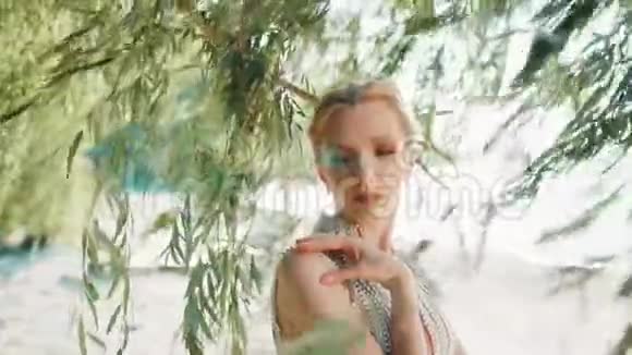 美丽的童话公主在靠近树叶的海边轻轻地把手放在她的肩膀和脖子上视频的预览图
