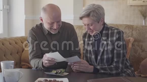 成熟的夫妇坐在沙发上检查他们的旧照片并分享他们的记忆家庭关系慢动作视频的预览图