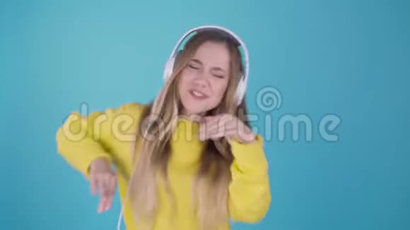 时尚酷笑女孩听音乐戴着黄色毛衣蓝色背景耳机4k视频的预览图