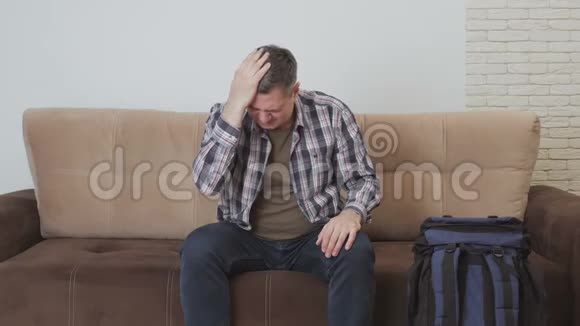 一位中年男子坐在沙发上双手捂住头头痛沙发旁边有一个视频的预览图