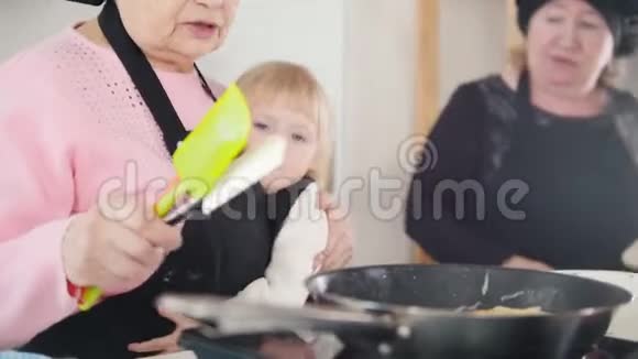 一位老妇人在明亮的厨房里做煎饼拥抱一个小女孩视频的预览图