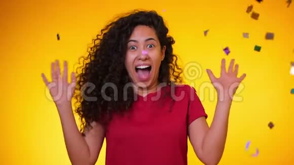 年轻的拉丁女孩卷发跳舞在黄色背景下的纸屑雨中玩得很开心女人庆祝视频的预览图