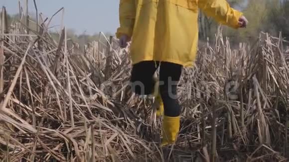 年轻女孩穿着黄色的靴子和外套在沼泽里小心翼翼地行走视频的预览图
