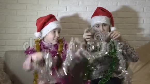 圣诞老人的帽子里有趣的孩子们用五颜六色的圣诞花环互相装饰坐在那里玩耍微笑视频的预览图