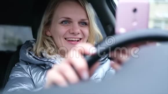 年轻女性博客写手穿着冬天的衣服坐在车里和追随者聊天现场直播寻找智能手机视频的预览图