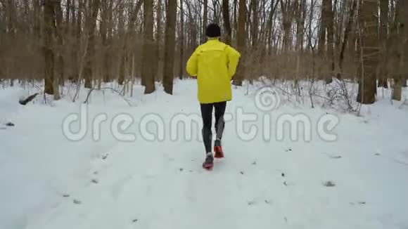 冬日雪地小道上运动男子在森林中奔跑的追踪镜头视频的预览图