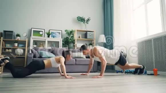快乐的年轻夫妇女孩和男人在公寓里做俯卧撑和拍手视频的预览图