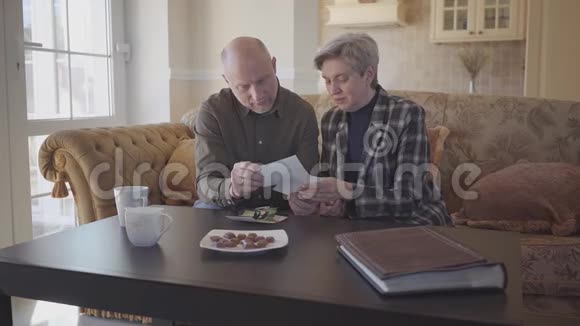 一对成年夫妇坐在沙发上检查他们的旧照片并分享他们的记忆家庭关系慢动作视频的预览图