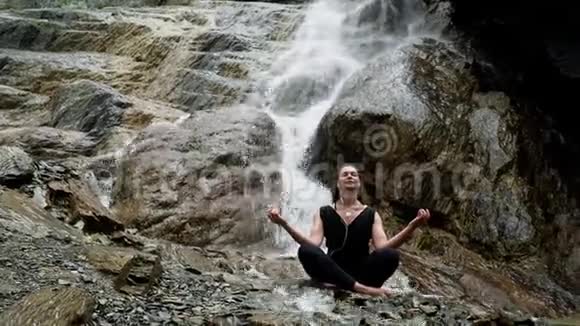 戴着耳机在瀑布边练习瑜伽的女人视频的预览图
