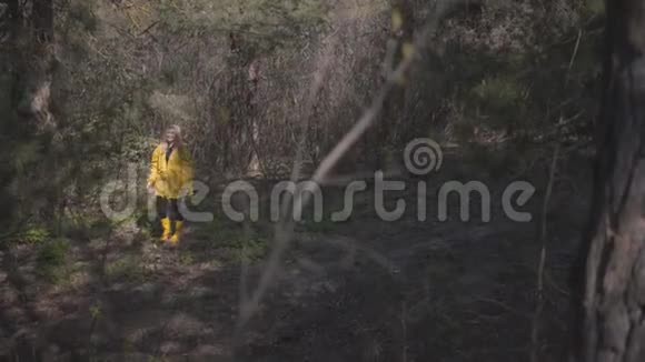 美丽的年轻快乐的女孩穿着黄色雨衣和黄色橡胶靴在大自然中行走女孩笑得很开心视频的预览图