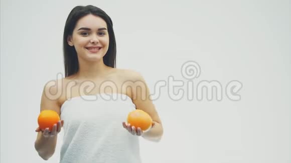 站在白色背景上的年轻漂亮女孩手里拿着橘子看着镜头很漂亮视频的预览图