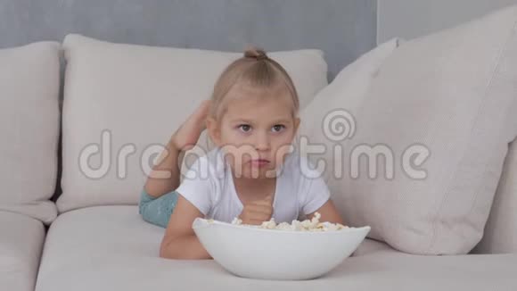 一个小女孩在软榻上吃着爆米花看着电视屏幕视频的预览图