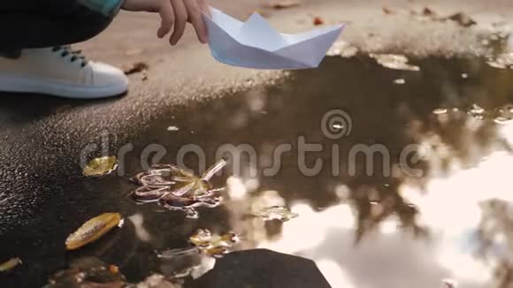 可爱的女孩在秋天公园的水坑里玩纸船童梦和旅行理念生活方式视频的预览图